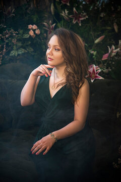 portrait of a beautiful brunette smiling woman  in vintage room with flowers and smoke in dark green long dress