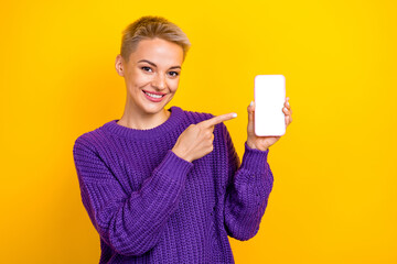 Portrait of attractive positive woman with short hair dressed violet sweater directing at smartphone isolated on yellow color background