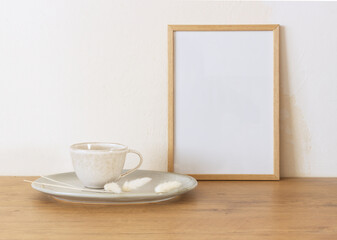 Horizontal white frame mockup on a vintage wooden bench, table, ceramic mug, and saucer with dry Lagurus ovatus grass. White wall background. Scandinavian interior. Selective focus.