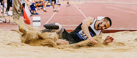 disabled athlete landing in sand on athletics competition