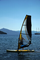 A man on a windsurf in the bay with a yacht in the background. Man learning to windsurf in the bay....