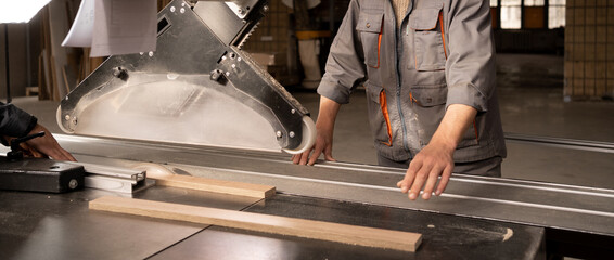 Male craftsman saws wood on a circular saw, carpenter saws wood on a saw machine in furniture...