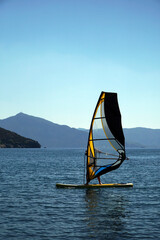 A man on a windsurf in the bay with a yacht in the background. Man learning to windsurf in the bay....