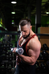Fototapeta na wymiar A brutal muscular man with a beard and a ponytail does a biceps exercise in the gym