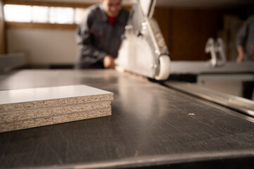 Carpenter working with sliding panel saw and sawing mdf board or fibreboard at furniture factory...