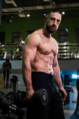 Plakat A brutal muscular man with a beard and a perfect body holds a dumbbell in his hand in the gym. Fitness, beauty