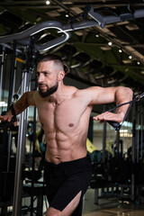 Fototapeta na wymiar A brutal muscular man with a beard and a perfect body does crossover exercises in the gym. Fitness, beauty