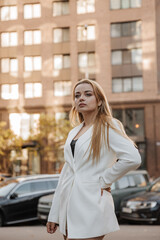 Blond stylish woman at oversized white jacket posing at the city background