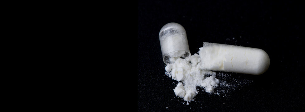 Close up view of probiotic capsules with white powder on black background. Space for text.