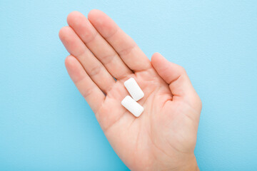 Young adult woman palm holding and showing white chewing gum pads on light blue table background....
