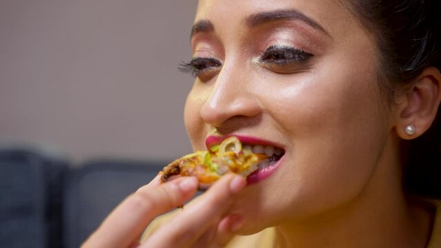Close up head shot of girl enjoys eating tasty pizza by closing eyes - concept of yummy food, delighted and positive emotion.