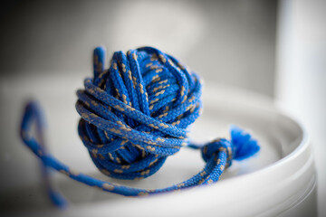 Knot of a blue polyester cord on the white plate. Blurred background. Close up view.