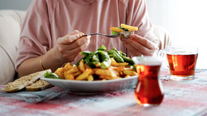 Woman puts fried potatoes and fried green long pepper to the bread with fork, turkish tea, traditional turkish breakfast, selective focus