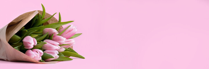 Beautiful delicate bouquet of tulip flowers in craft wrapping paper on pink background banner. Panoramic web header with copy space. Wide screen wallpaper
