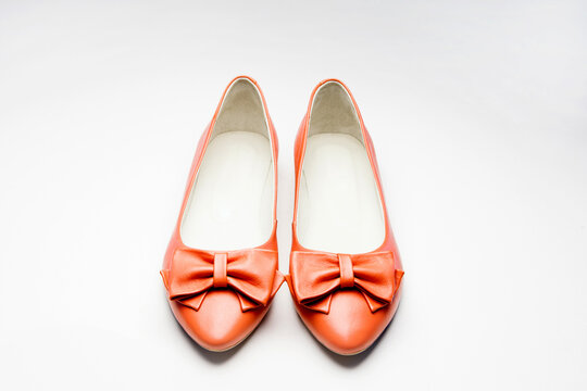 A pair of women's leather shoes with a bow tie, red, without heels, lie horizontally on one, on a white background. close distance