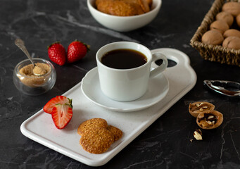 White cup of coffee on a saucer with strawberry biscuits, walnuts.