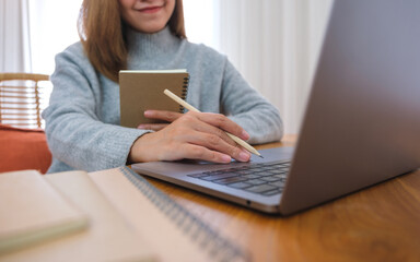 Closeup image of a young woman writing on notebook while working or study on laptop computer at home