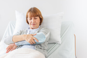 Senior woman suffering from shoulder pain at home in the living-room