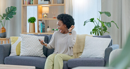 African woman celebrating a new job while sitting at home on a couch. A young females loan is...