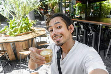 young latino man with dreadlocks taking a selfie portrait with a coffee in hand.