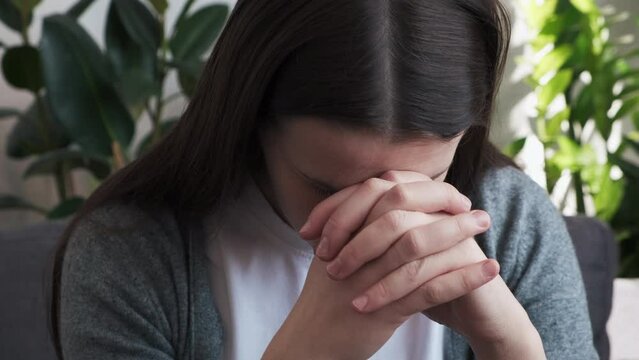 Worried woman think of overcoming bad life event ponder on hard decision. Critical situation concept. Thoughtful young girl sit on sofa lean forward on folded hands try to keep emotions under control