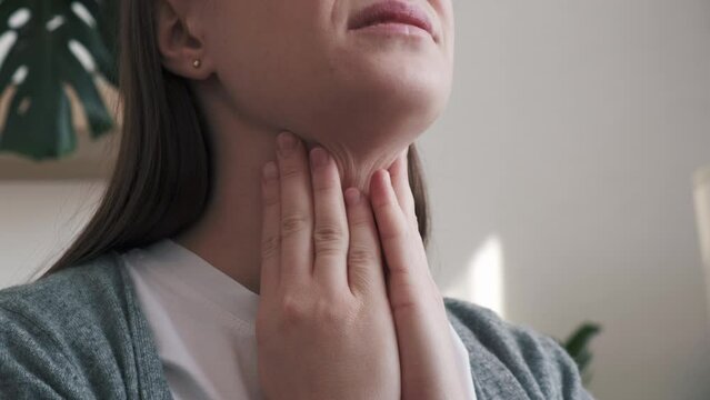 Close up of unhealthy sad young brunette woman holding hands over sore throat feeling discomfort. Painful neck and frowning, thyroid disorders, suffering sore throat, tonsils inflammation concept