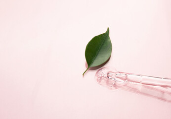 Pipettes with a cosmetic product on a pink background and green leaf. Copy space