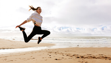 Young fit lady jumping high on beach ocean, active european woman working out outdoors, panorama with copy space