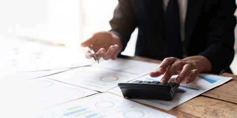 Close up Business man using calculator and laptop for do math finance on wooden desk in office and...