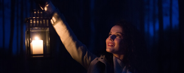 Fototapeta na wymiar A young smiling woman in the woods walking with a lantern at night