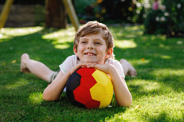 Happy active kid boy playing soccer with ball in German flag colors. Healthy child having fun with football game and action outdoors