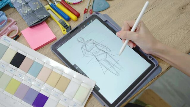 Hand Fashion designer woman draws sketches for a new fashion design, draws on an electronic tablet fashionable clothes. Close up female actively working workspace