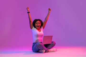 Euphoric Black Female With Laptop Celebrating Success In Neon Light