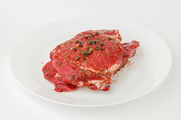 Marinated raw meat with spices on a white plate.