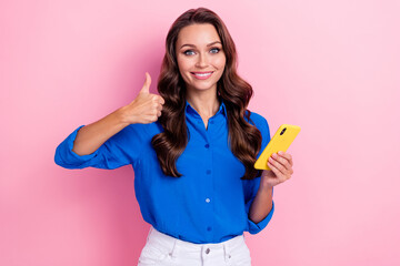 Portrait of good mood sexy pretty girl wavy hairstyle wear blue shirt show thumb up like hold phone isolated on pink color background