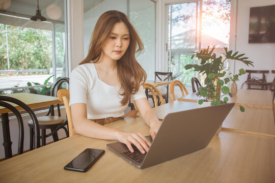 Young smart asian woman freelance online working from cafe with Laptop computer and smart phone. Female working remotely at coffee shop. Concept of networking or remote work. Global business network.
