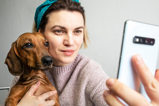 A young woman taking selfies or talking on a video link with a dog in her arms.