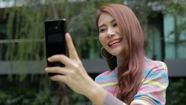 Cheerful Asian beautiful woman happy She uses her smartphone to video call online in the outdoor garden of her modern apartment. Housing concept. city ​​living