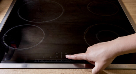 A woman's finger presses the inclusion of a modern induction hob in the kitchen. Electric induction...