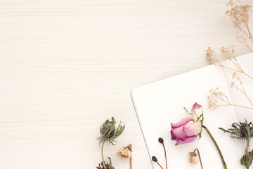 White notebooks, roses and other dried flowers and copy space on a white wooden table