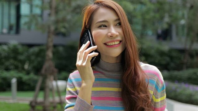 Cheerful Asian beautiful woman happy She walks on the phone talking in the outdoor garden of her modern apartment. Housing concept. city ​​living