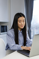 Beautiful Asian girl working on a laptop computer at home. Cheerful Vietnamese POC woman typing text on modern notebook pc keyboard