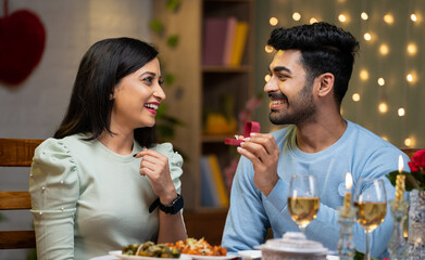 Happy young man proposing to girlfriend offering gold ring durin valentines day at candle light dinner at home - concept of asking a marriage, affection and gift or present.