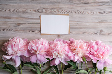Mock up blank white paper card for text and delicate peonies on a wooden background. Flat lay, top view. Place for text. Greeting card