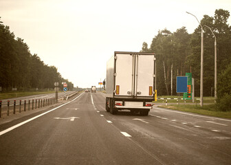 A truck with a white semi-trailer transports cargo on a highway. Trucking as a business, industry. Copy space for text, toned
