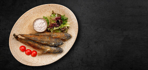 Fried goby fish in a plate, on a dark concrete background