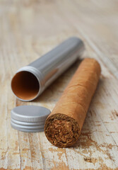 Handmade tobacco cigar on wooden desk with empty aluminium tube macro.