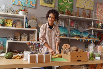 Smiling woman is packing handmade candles for selling in own home decor studio