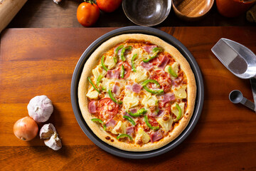 Top view of fresh baked homemade pizza on wooden table with ingredients and spices. Delicious Italian pizza is ready for deliver. Hawaiian Pizza with bell pepper bacon and pineapple.