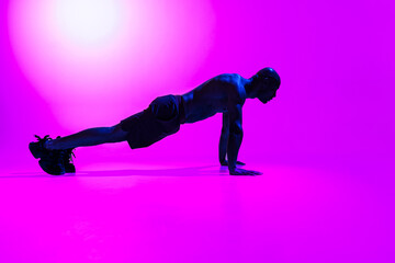 Fototapeta na wymiar Athlete in plank position does push-ups and arm exercises on studio background